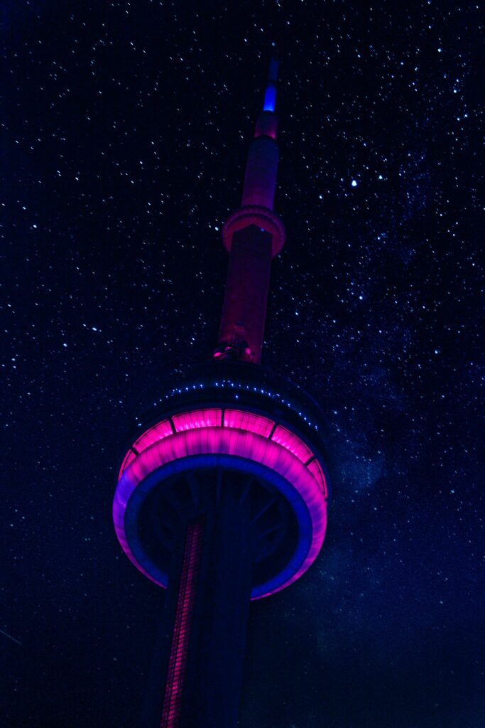 Low angle view of CN Tower illuminated with vibrant lights against a starry night sky in Toronto, Canada.